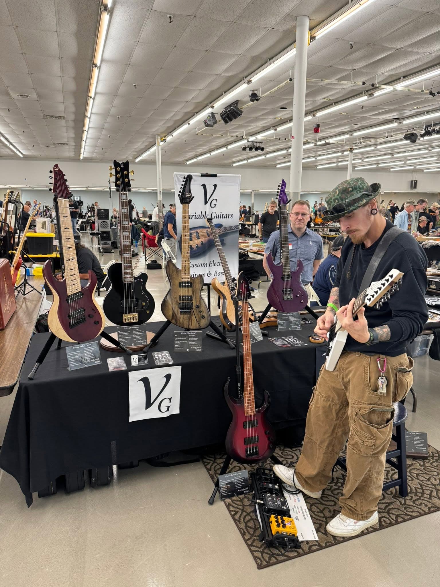 An attendee trying a white electric guitar at a vendor table of custom instruments