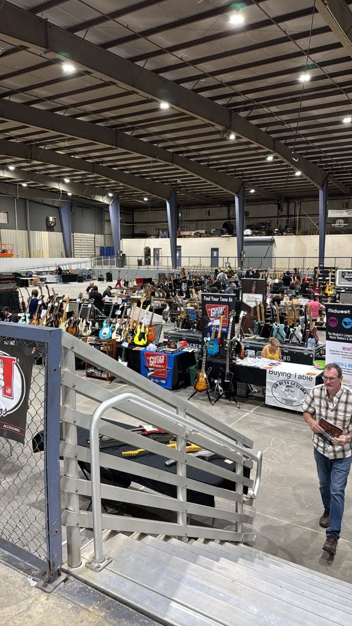 The Guitar Fest floor from the stairs — aisles of vendor tables packed with guitars